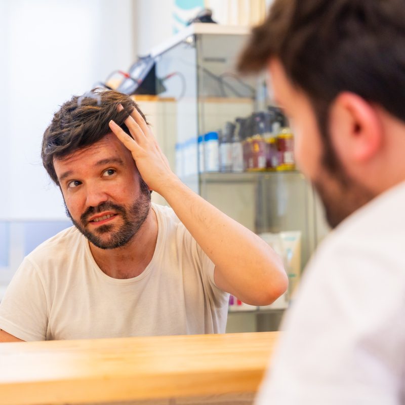 Reflection in the mirror of a satisfied bald man with capillary prosthesis looking into hair salon mirror