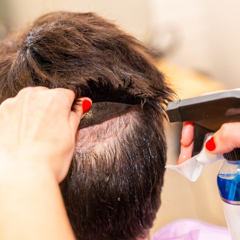 Close-up photo of the hands of a hairstylist removing the capillary prosthesis of a man in the hair salon