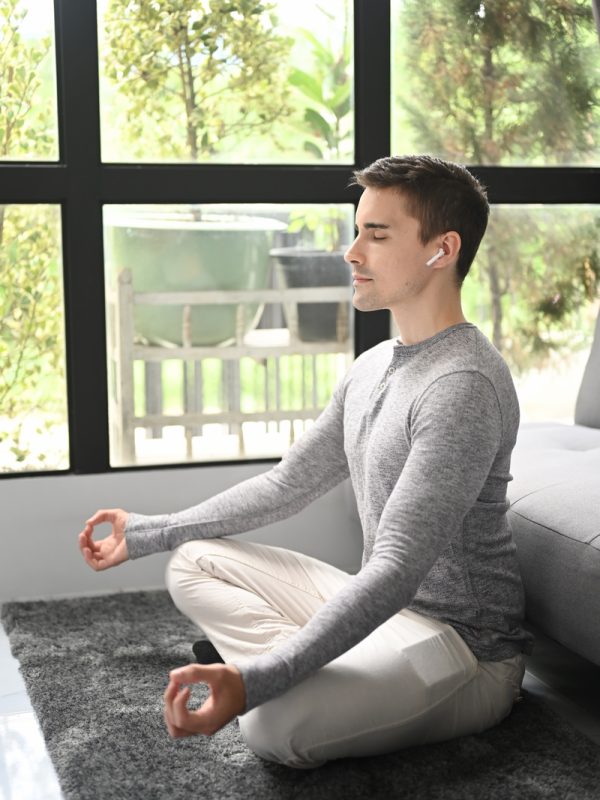 Young healthy man practicing yoga at home in lotus pose.